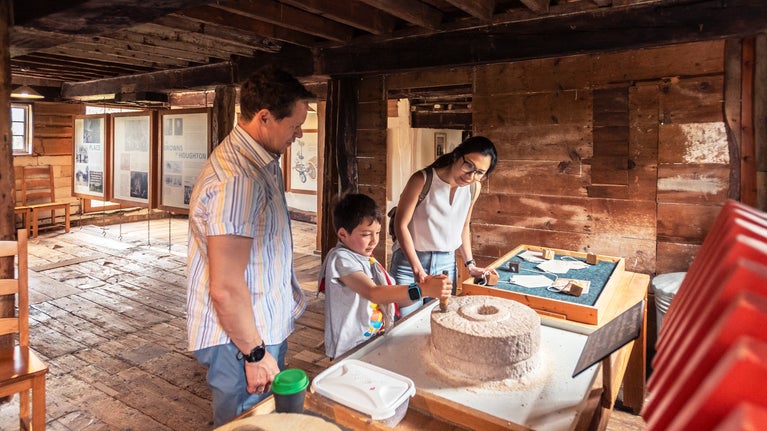 Visitors milling on a hand quern inside Houghton Mill